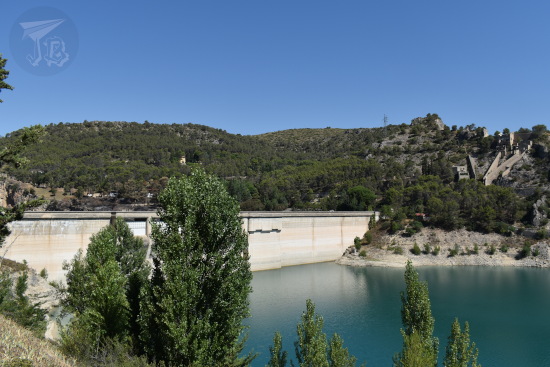 A white-grey dam closes the reservoir. There are trees in the foregrond and the water looks almost turquoise.